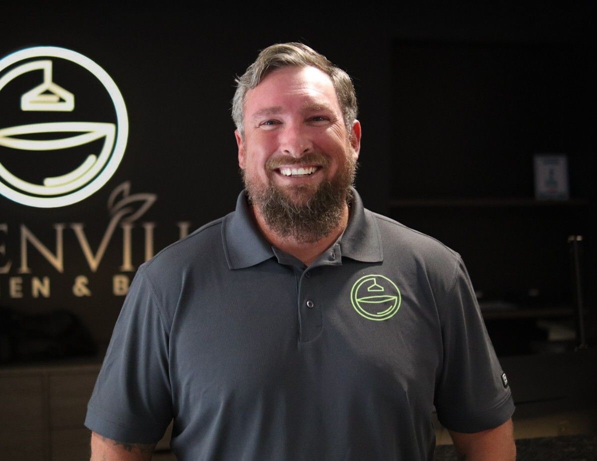 Smiling man in a gray polo stands in front of a business sign