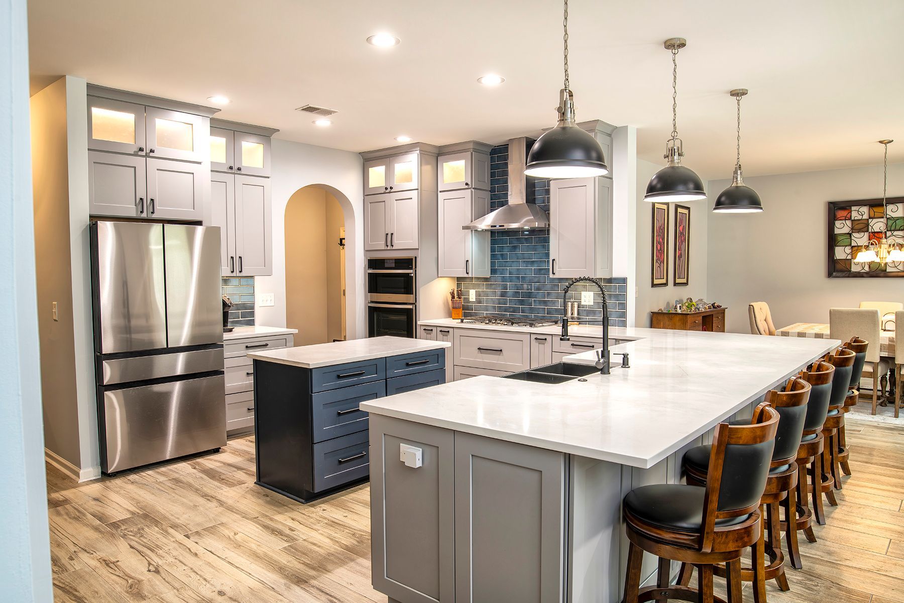 Modern kitchen with white island, blue cabinets, stainless fridge, and barstools under pendant lights