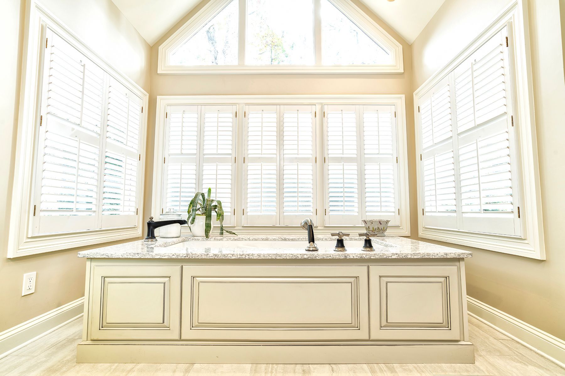 Bright kitchen sink area with cream cabinets, white shutters, and large windows filling the room with light