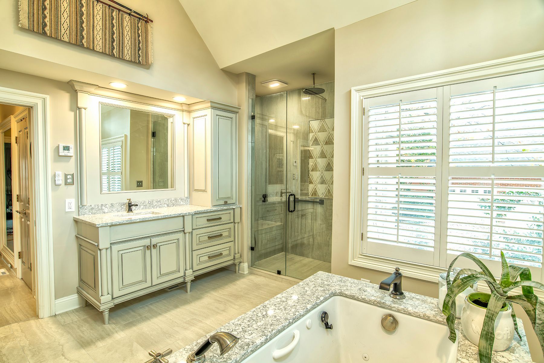 Bright luxury bathroom with vanity, glass shower, and large window beside a bathtub