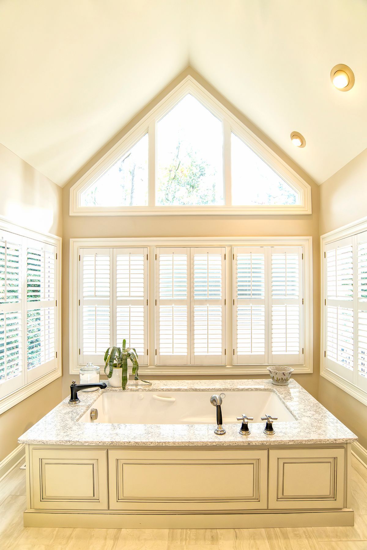 Bright cream bathroom with marble vanity, large windows, and a vaulted ceiling window.