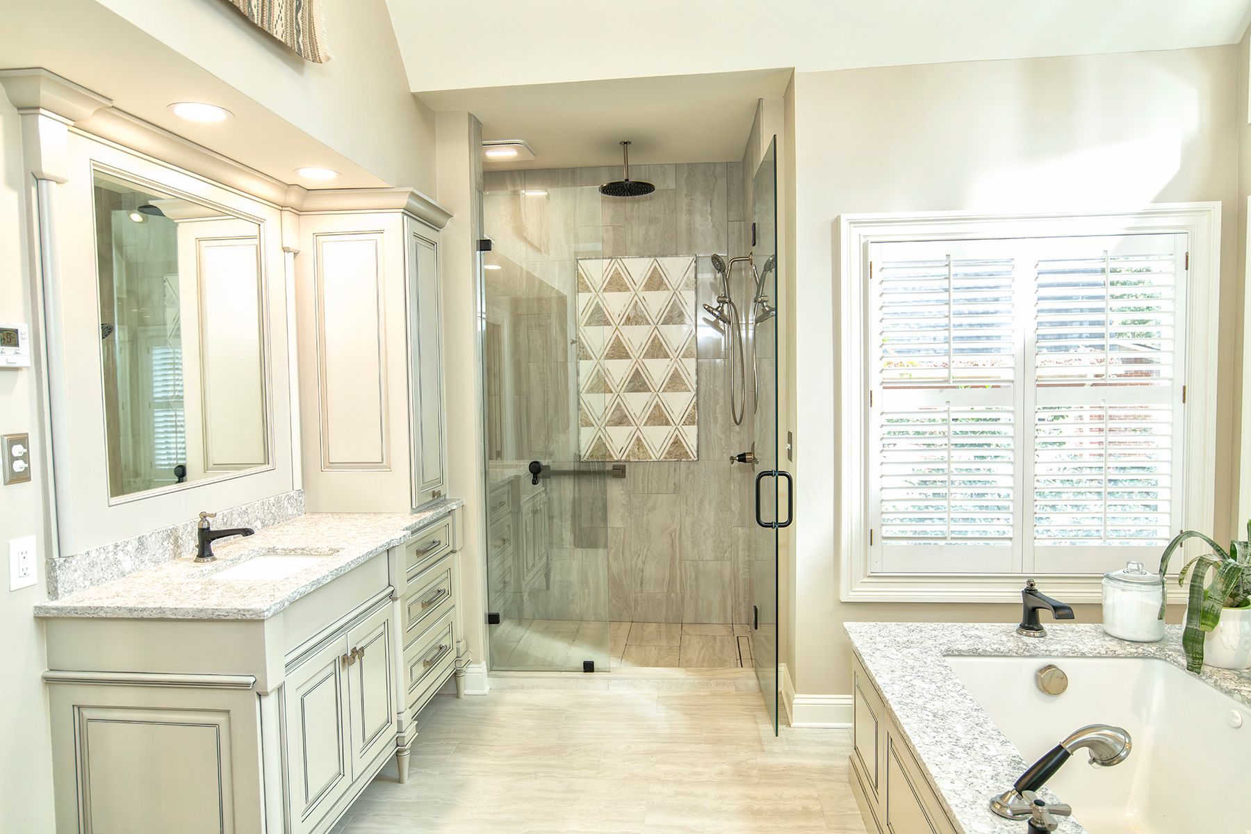Bright white bathroom with double vanity, mirrors, shower, and bathtub with window shutters