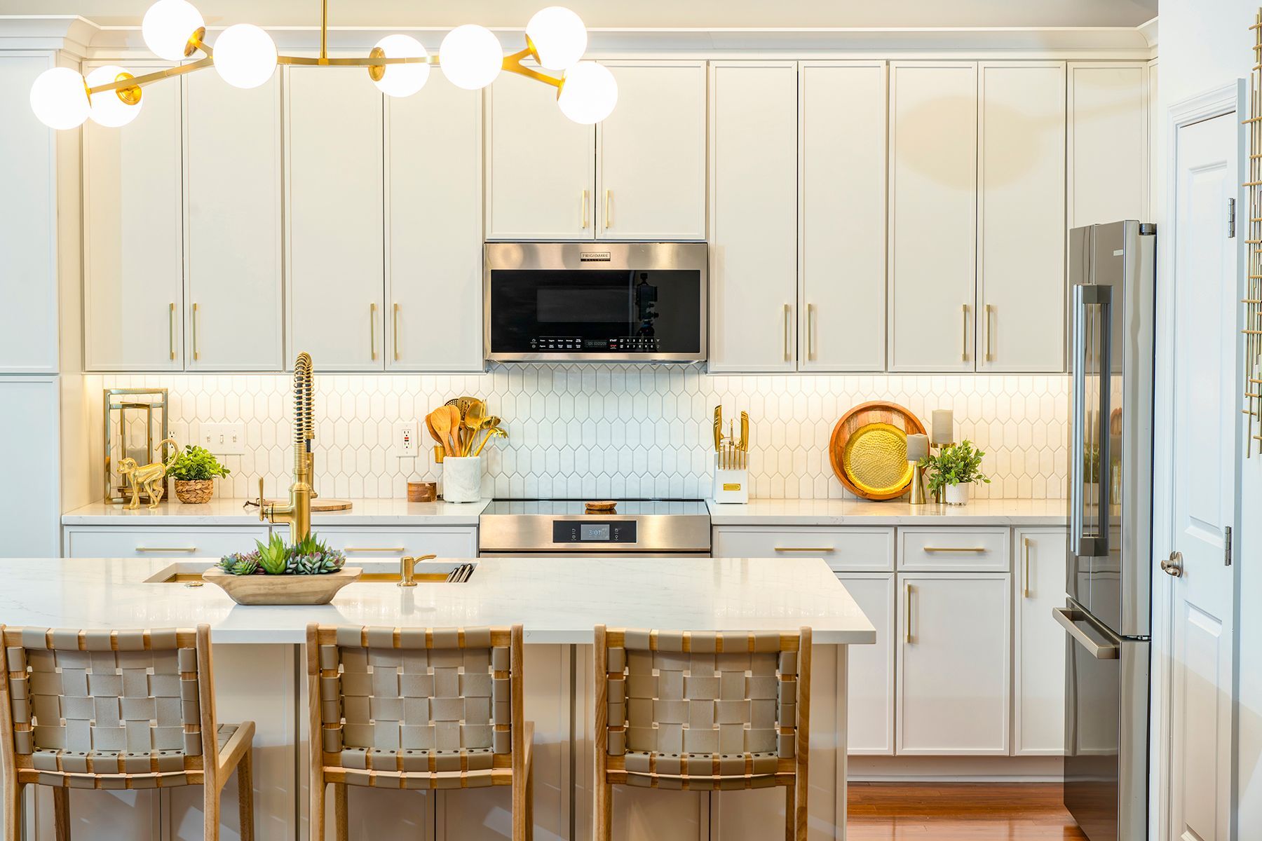 Bright white kitchen with island, wicker stools, and gold accents under pendant lights