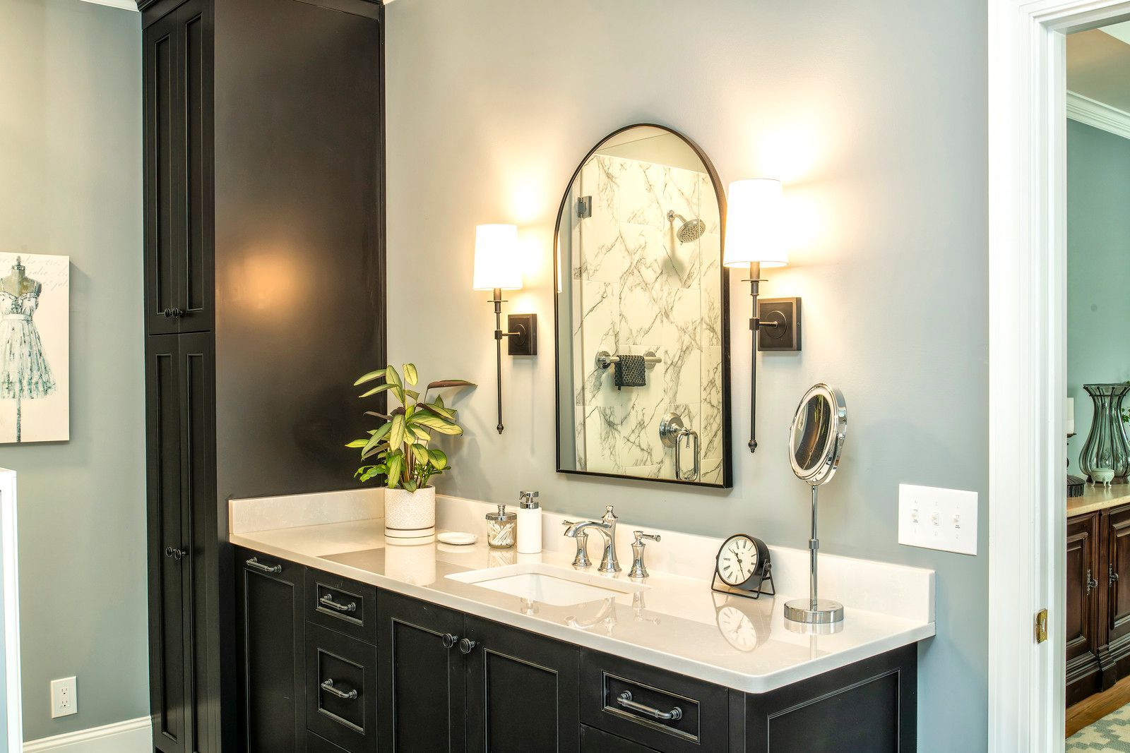 Modern bathroom vanity with black cabinets, white countertop, round mirror, and wall sconces