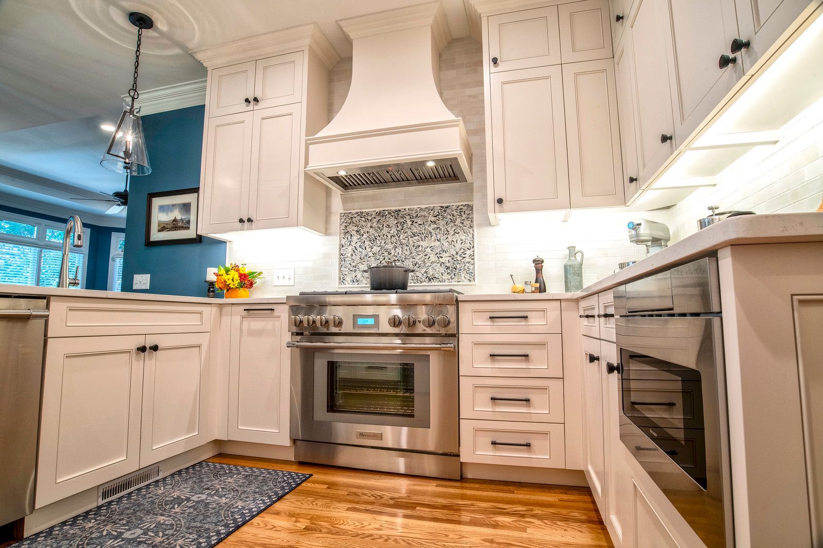 Bright white kitchen with stainless steel stove, mosaic backsplash, and blue accent wall.