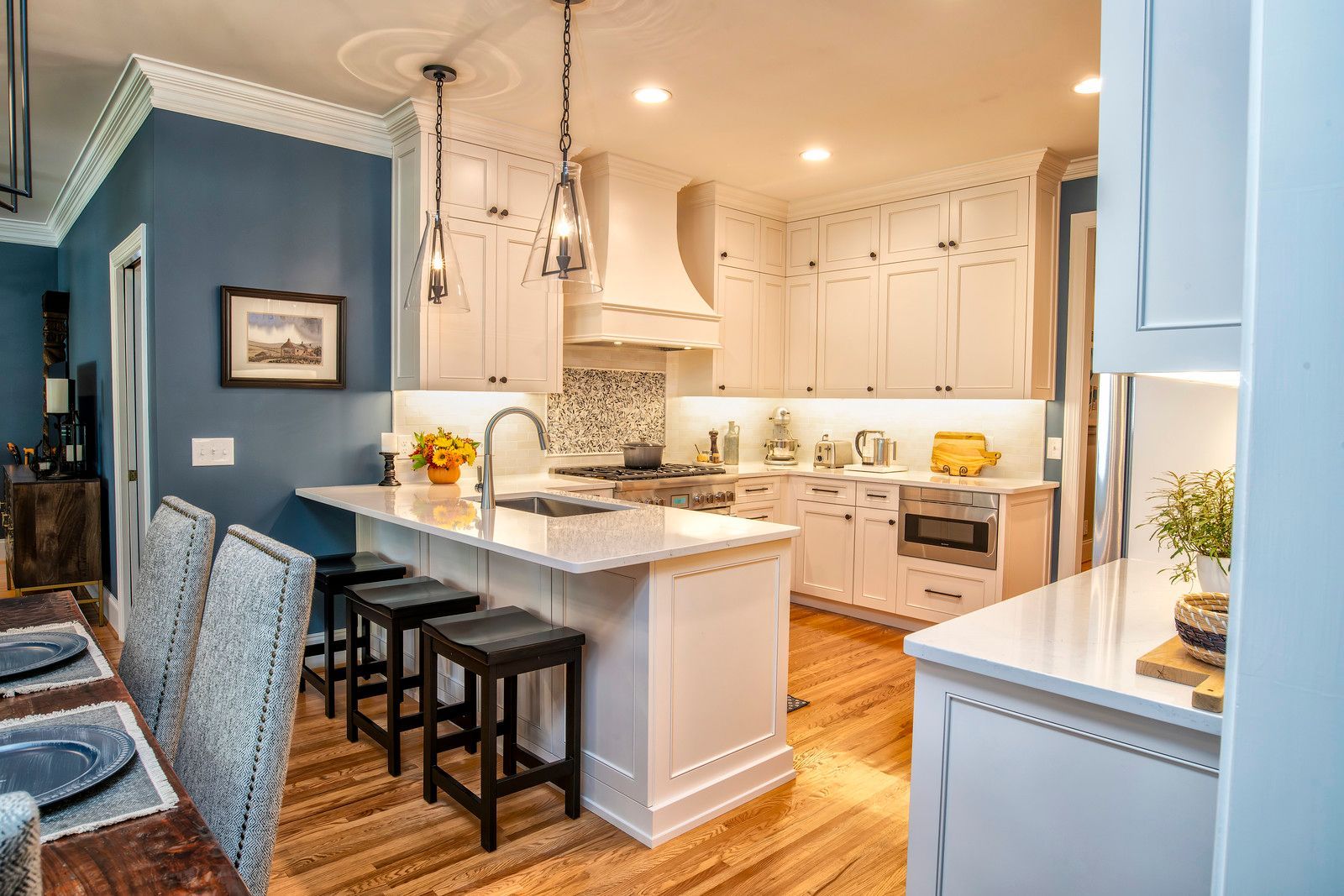 Bright kitchen with white cabinets, blue walls, granite island, and bar stools beside hardwood floors