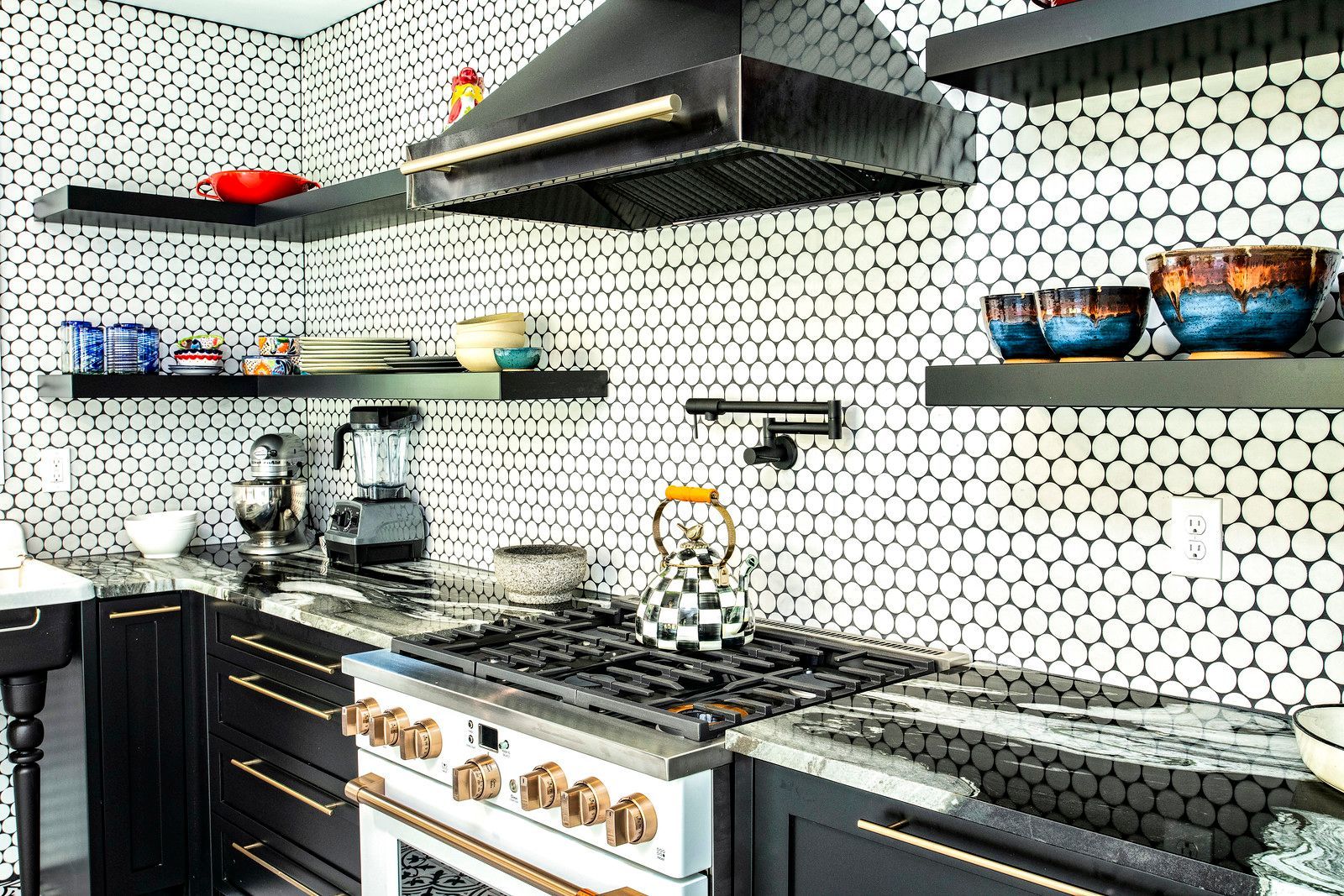 Modern kitchen with hex tile backsplash, black cabinets, white stove, and shelves with cookware and decor