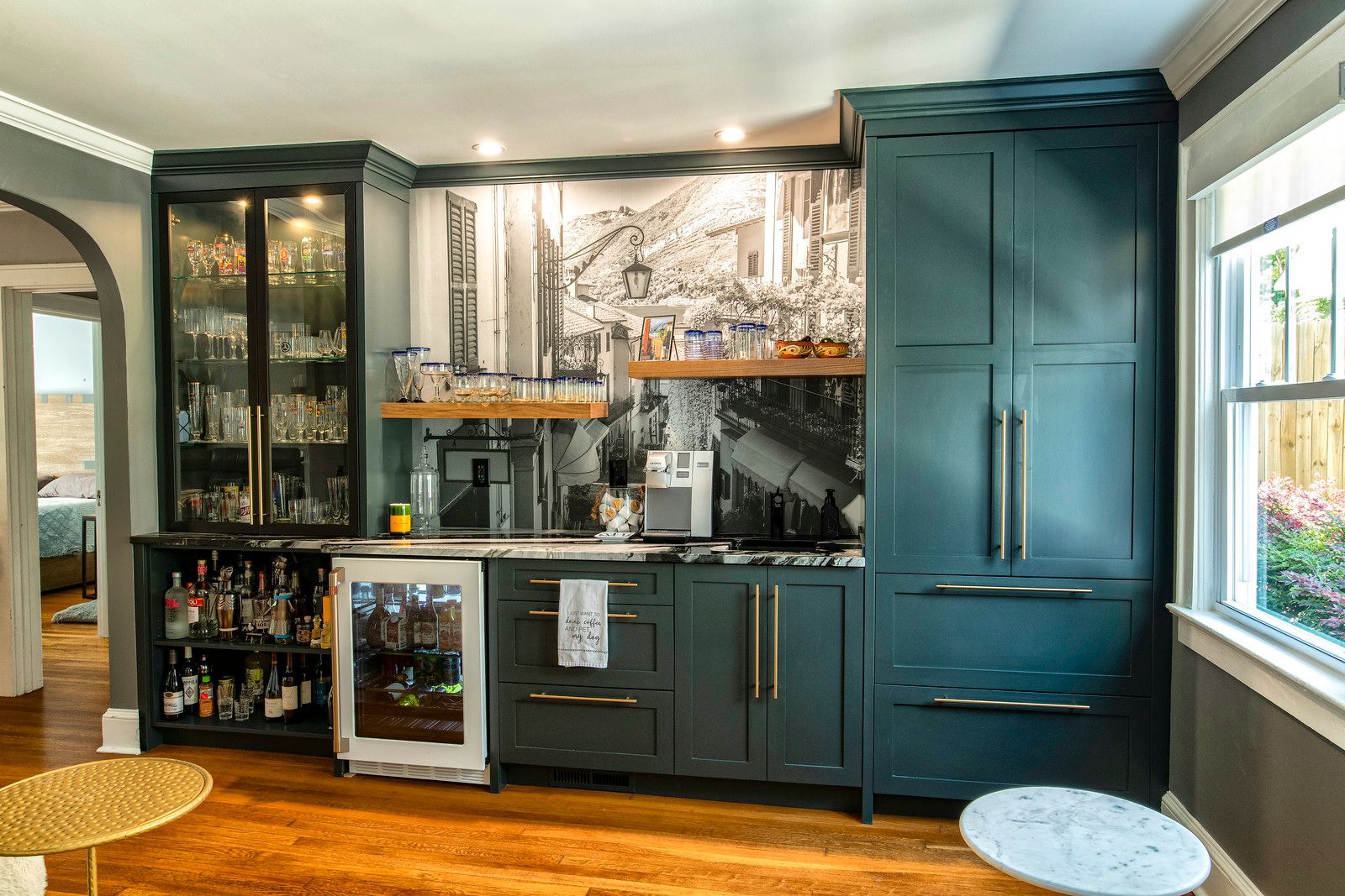 Stylish home wet bar with dark cabinets, glass shelving, wine fridge, and teal built-in storage.