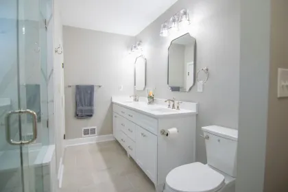 Bright white bathroom with vanity, mirror, toilet, glass shower, and towel rack