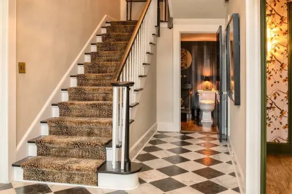 Hallway with carpeted stairs, checkered tile floor, and a bathroom visible at the end