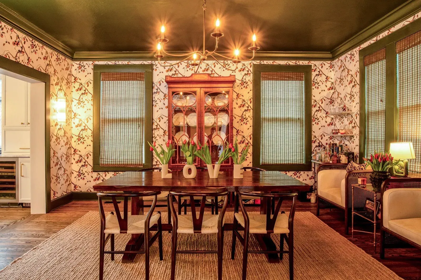 Vintage dining room with floral wallpaper, dark wood table and chairs, and green-framed windows
