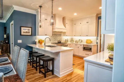 Bright blue and white open kitchen with island, bar stools, hardwood floors, and pendant lights