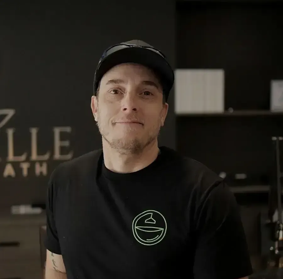 Person in a black cap and shirt standing in a dark room with a logo sign in the background