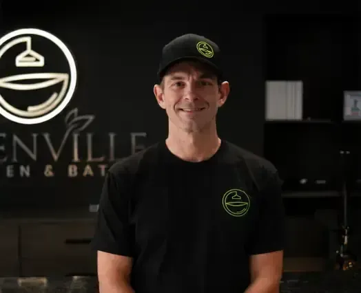Man in black shirt and cap standing in a brewery with a logo sign behind him