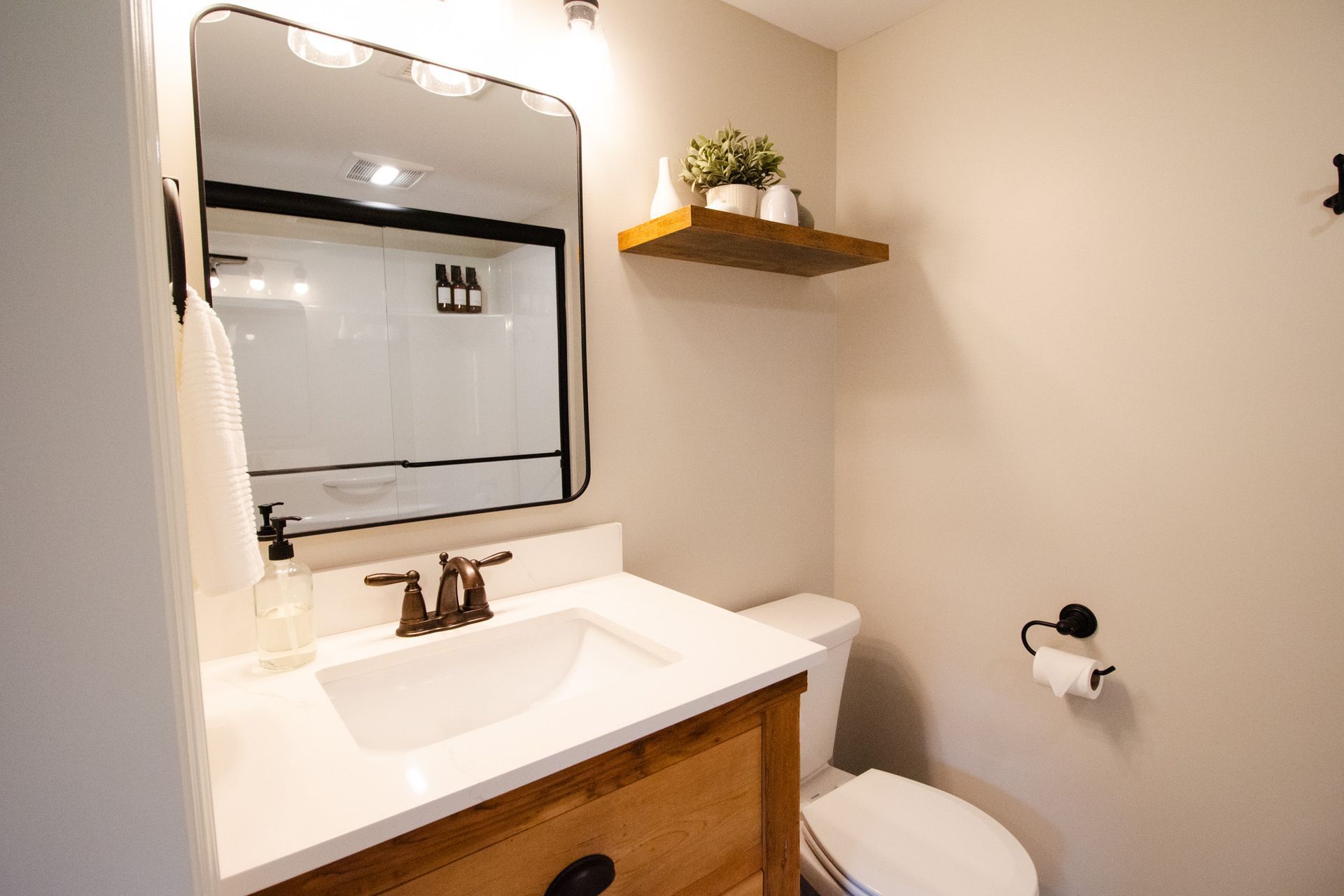 A bathroom with a sink , toilet , mirror and shelf.