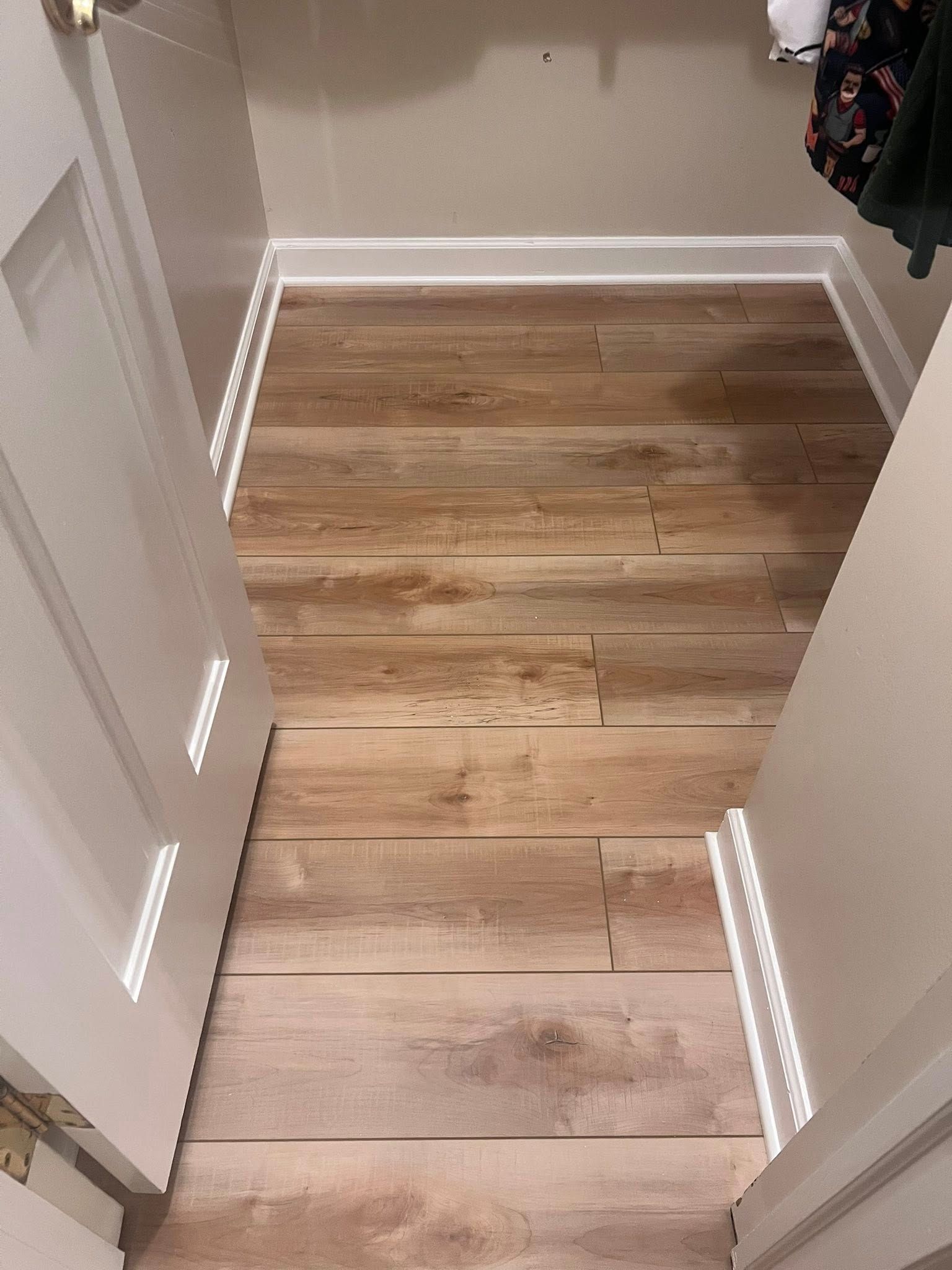 Narrow hallway with light wood flooring, white baseboards, and closed doors on both sides.