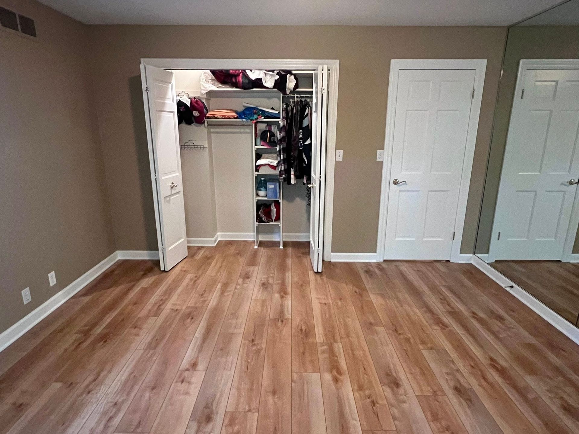 Empty bedroom with beige walls, wood floor, and two open closets.