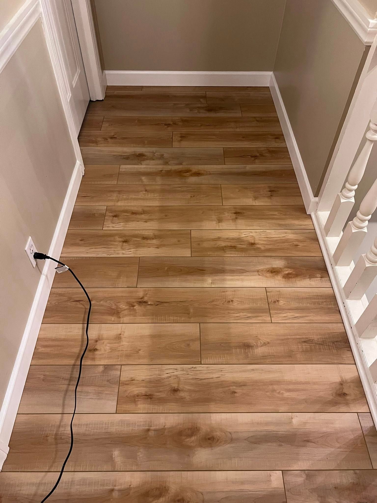 Narrow hallway with wood plank flooring and white trim, viewed from above; black cable on the left side.