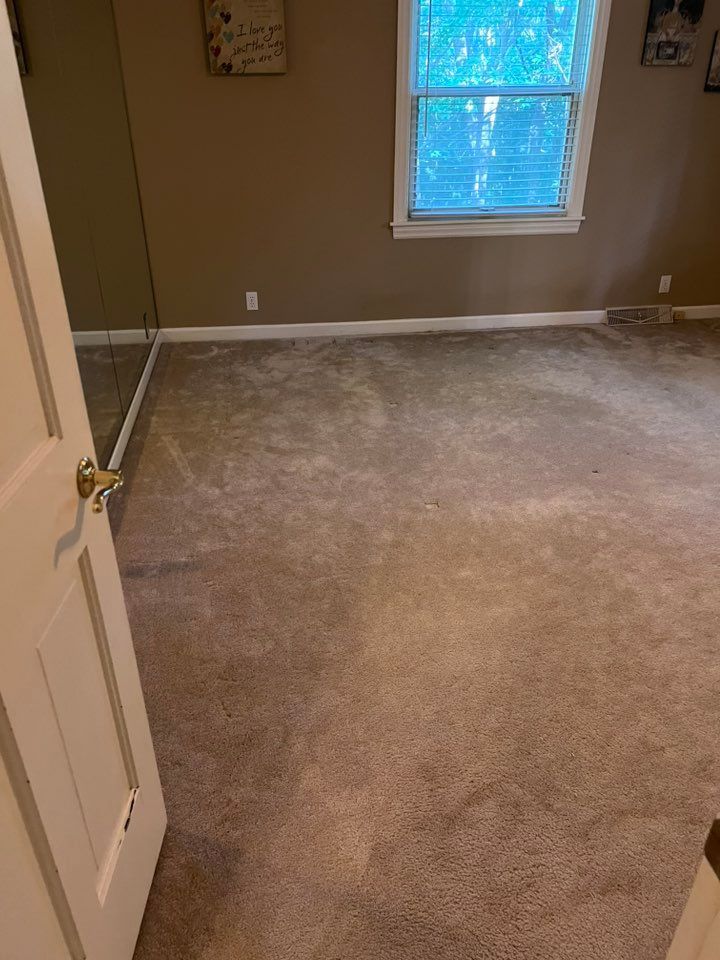 Empty beige carpeted room with a window and partially open door