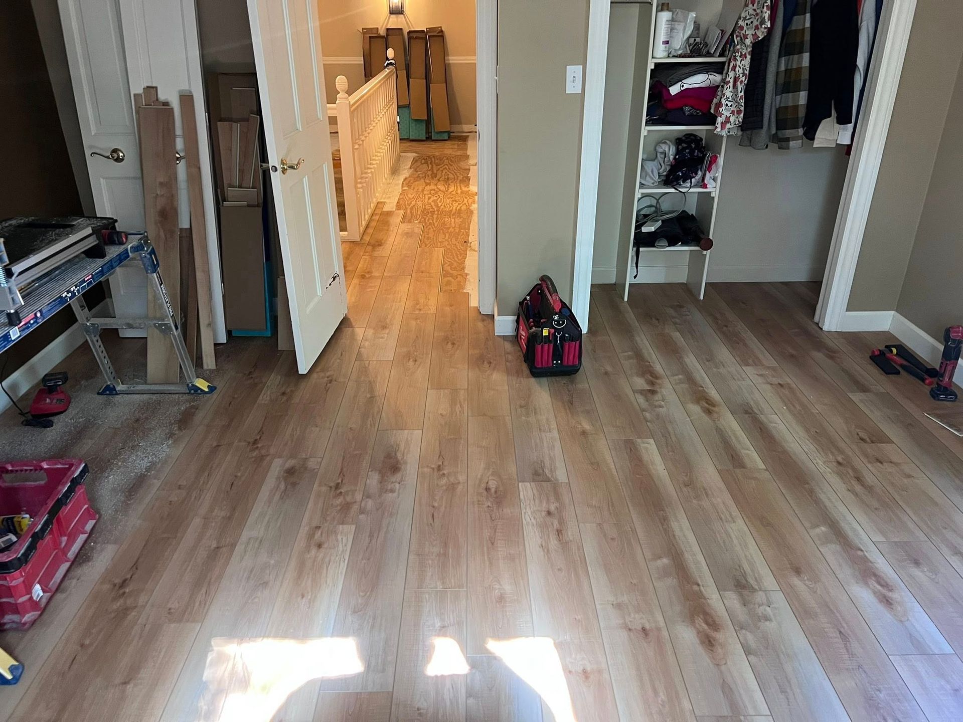 Empty room with wood floors, open closet, and a hallway leading to a lit back room