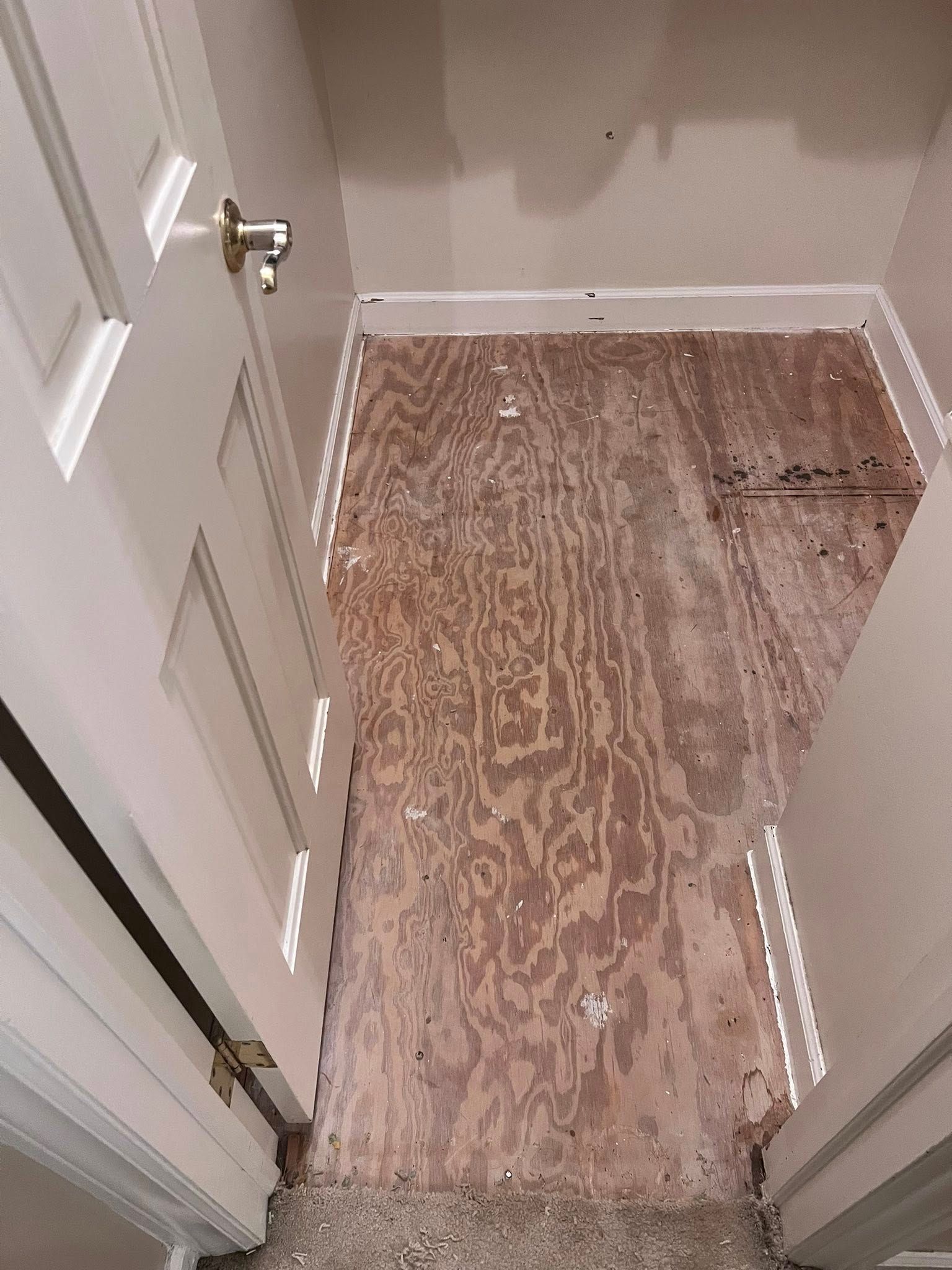 Narrow bathroom nook with plywood flooring and a small wall-mounted faucet.