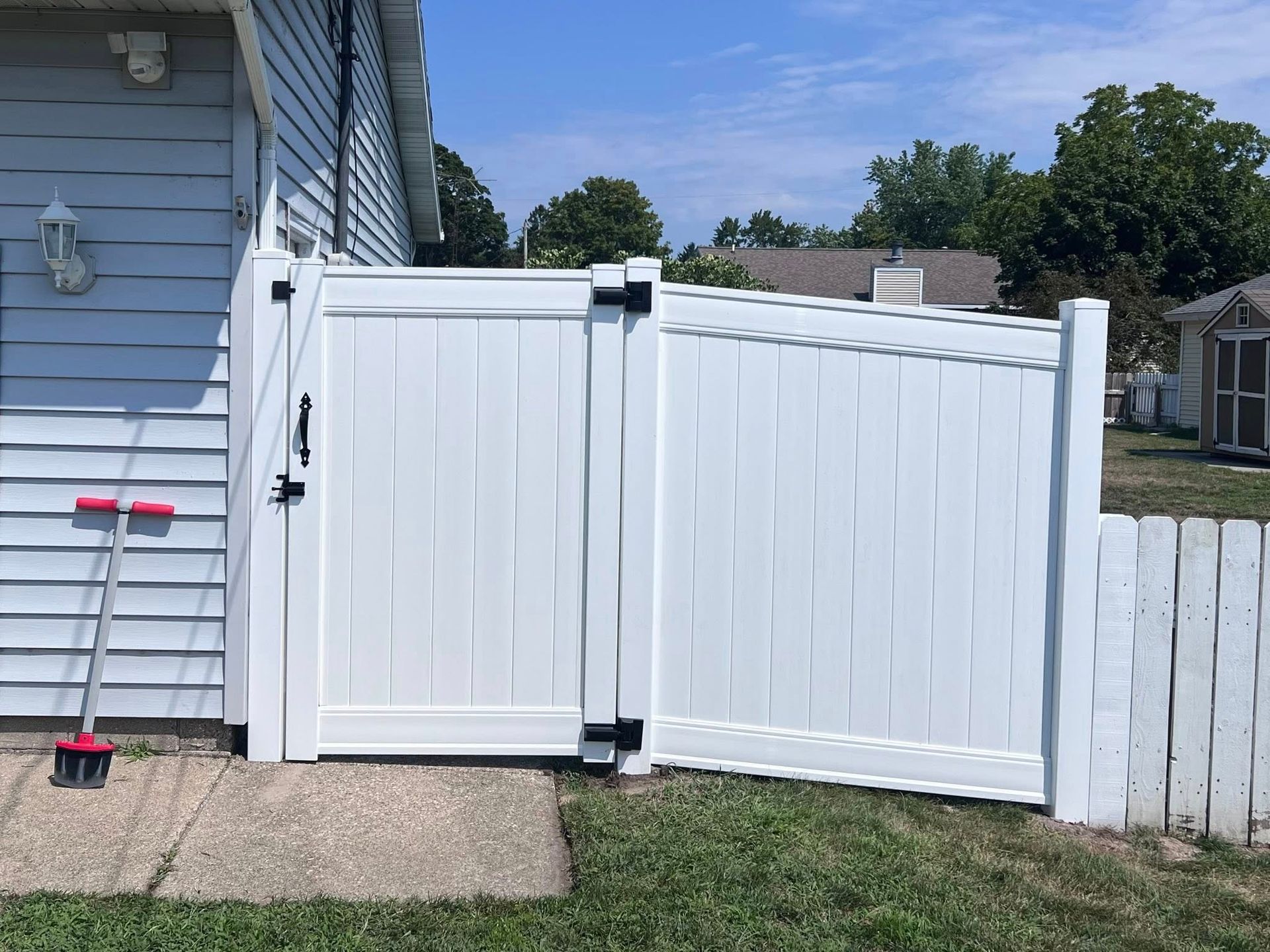White vinyl gate blocking a narrow side yard beside a light blue house, with fence and lawn.