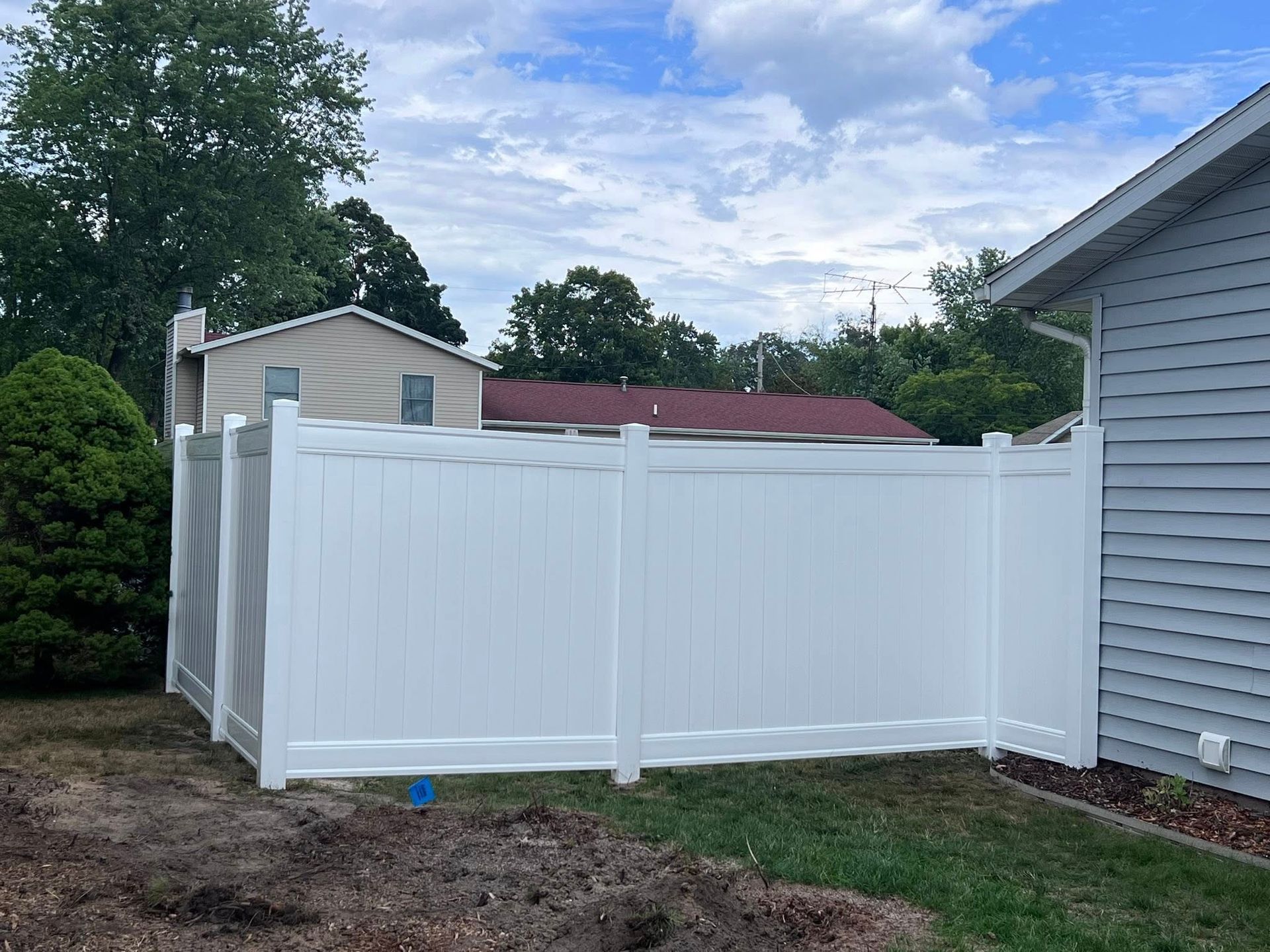White vinyl privacy fence enclosing a backyard beside a gray house under a cloudy sky