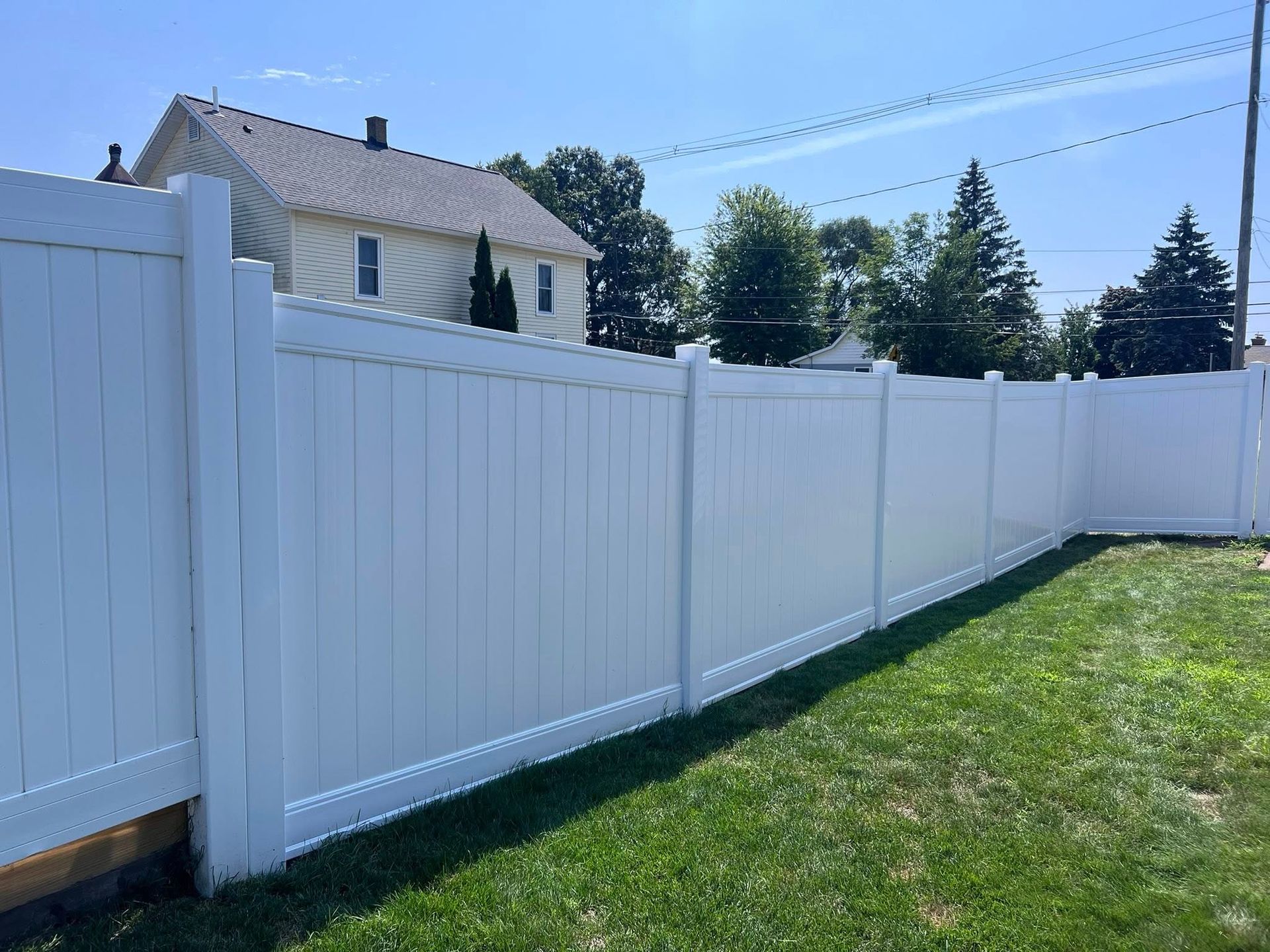 White vinyl privacy fence along a green lawn beside a house under a clear blue sky