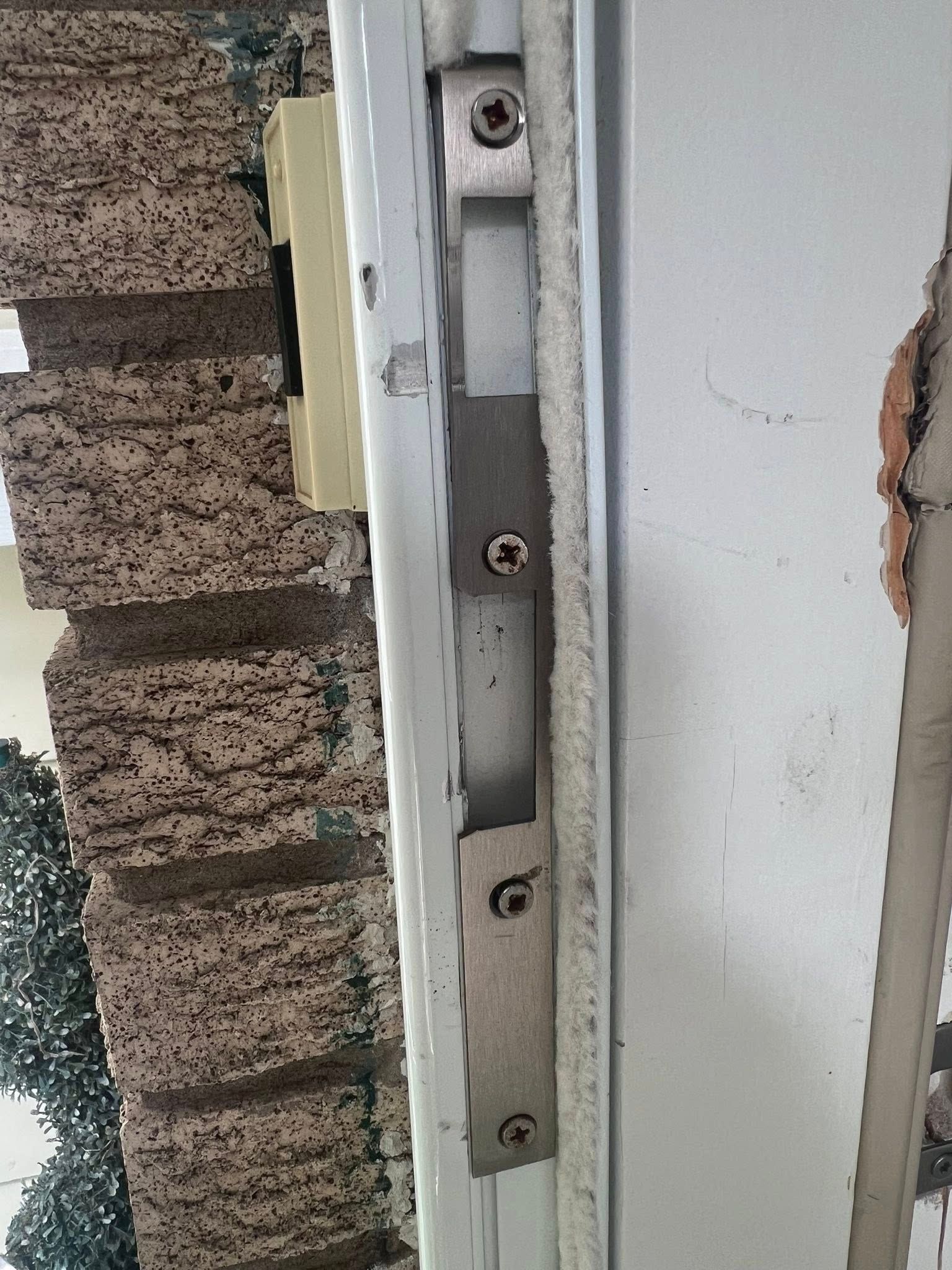 Close-up of a door latch on a white frame beside a rough brick wall.