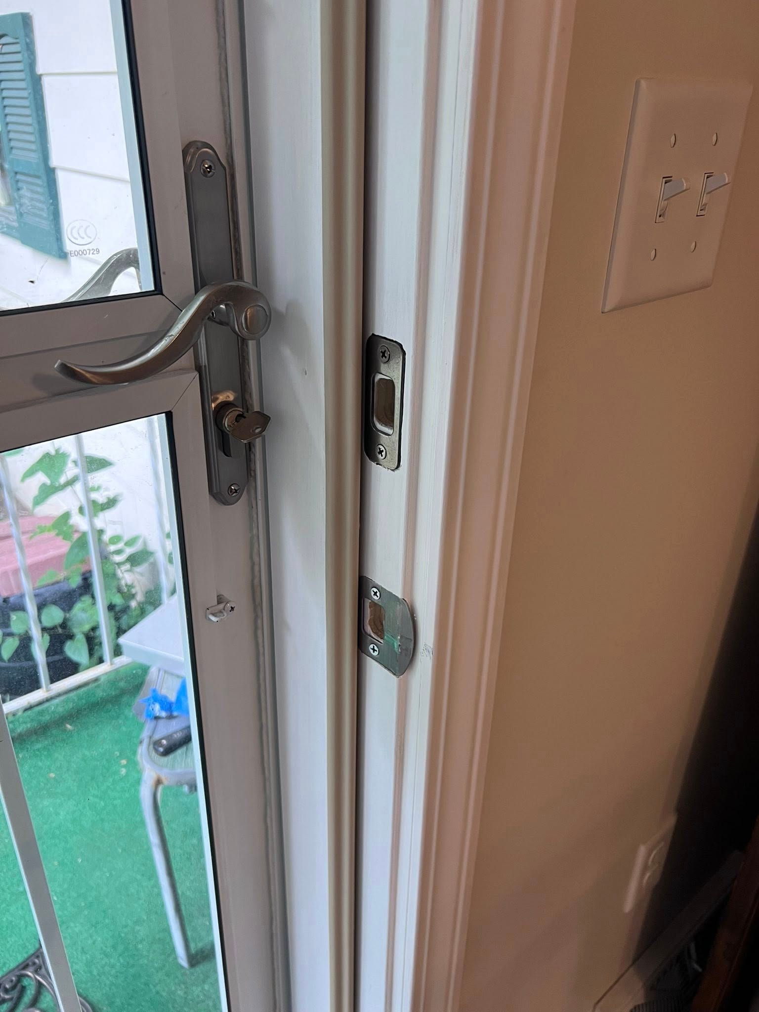 Close-up of a white door frame and silver lock hardware beside a glass door.