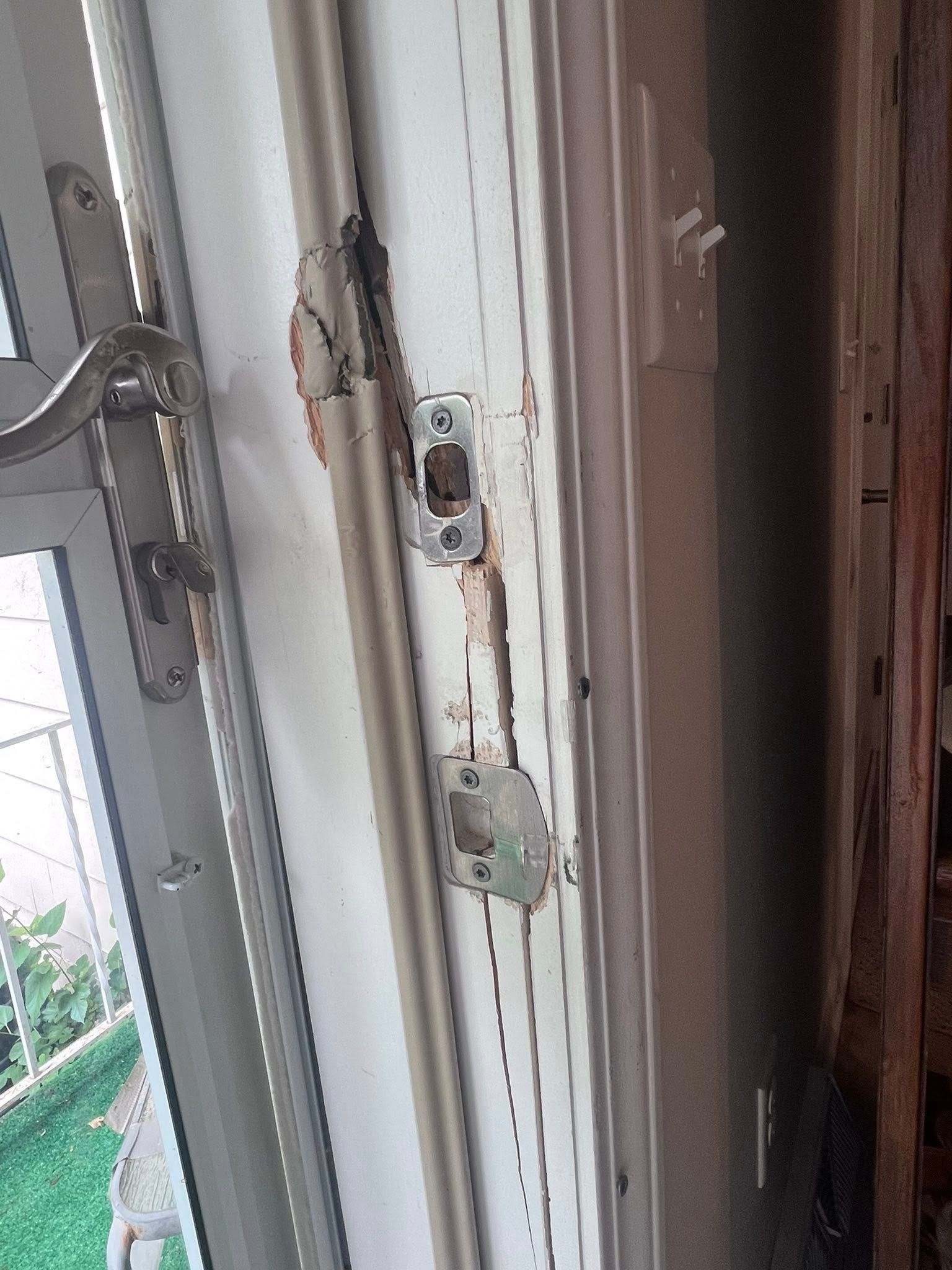 Close-up of a white door frame with a metal latch and lock hardware, showing peeling paint.