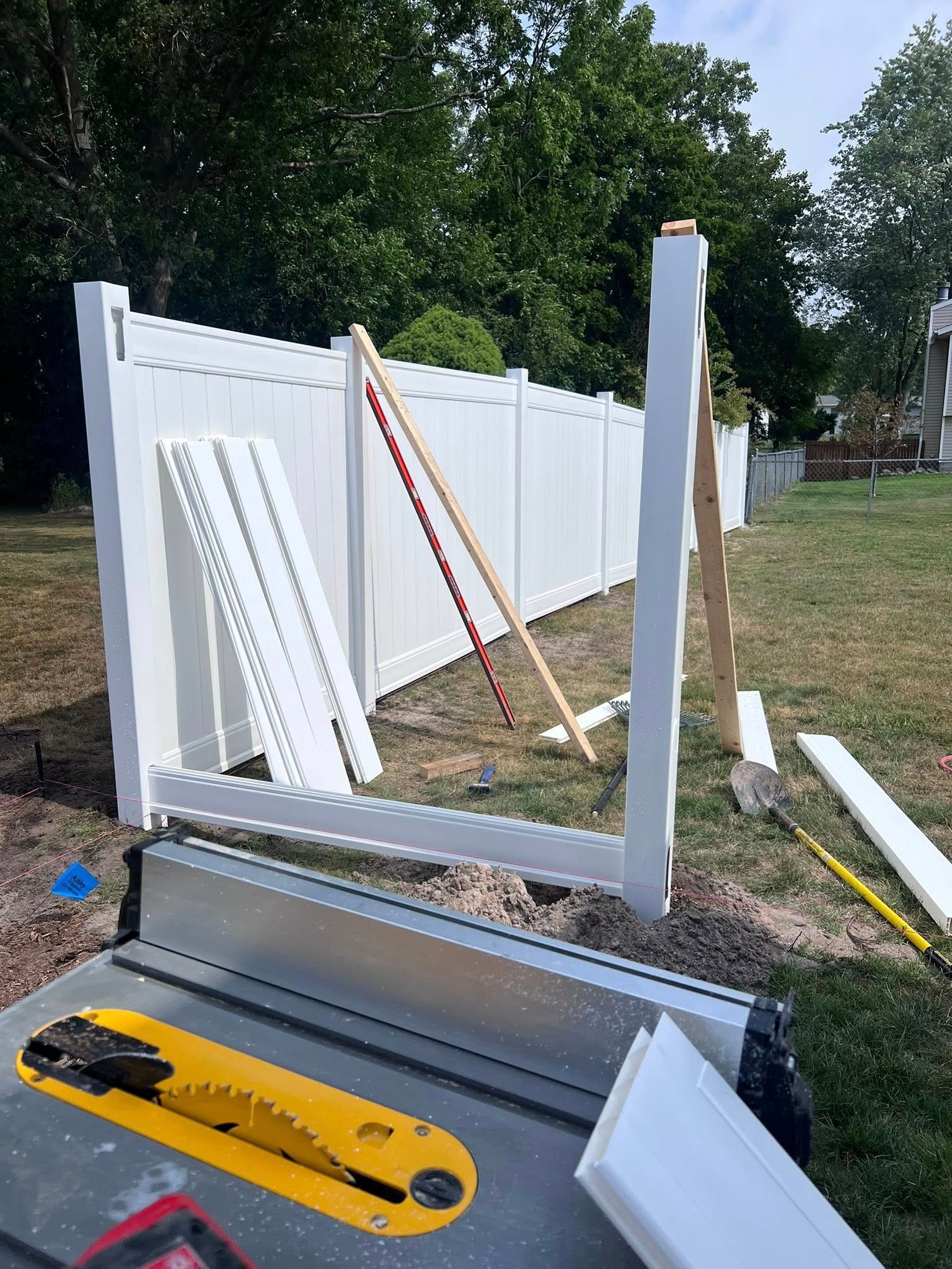 Disassembled white fence panels and posts on a sawhorse with tools in a backyard yard.
