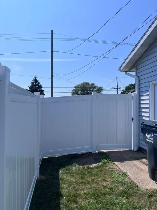 Backyard with white vinyl fence, small grass patch, house siding, and blue sky overhead