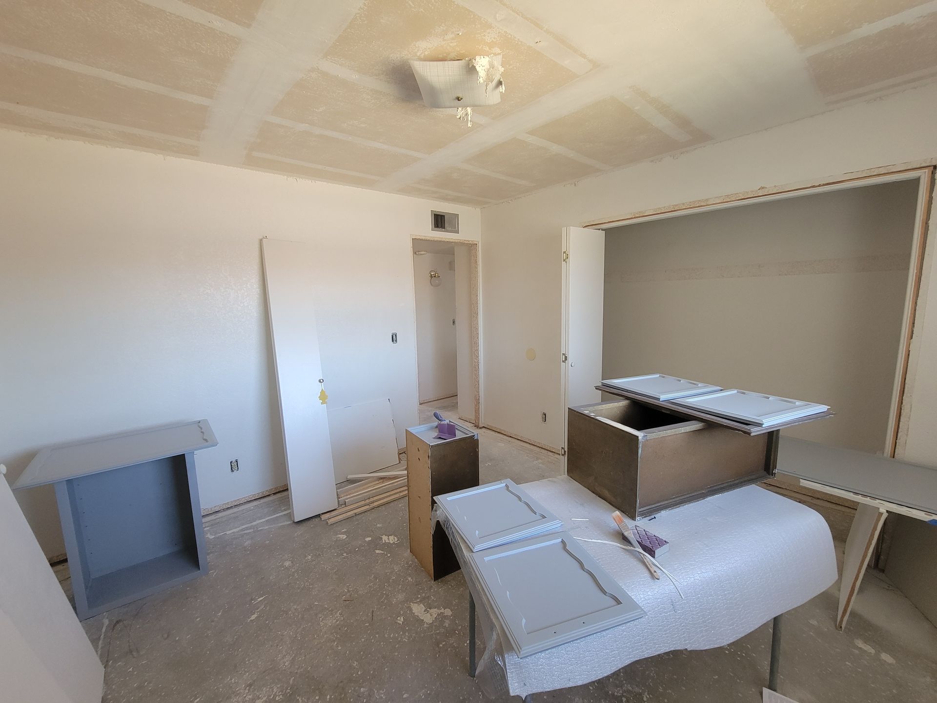 Unfurnished room with white walls, exposed ceiling patches, and scattered construction materials.