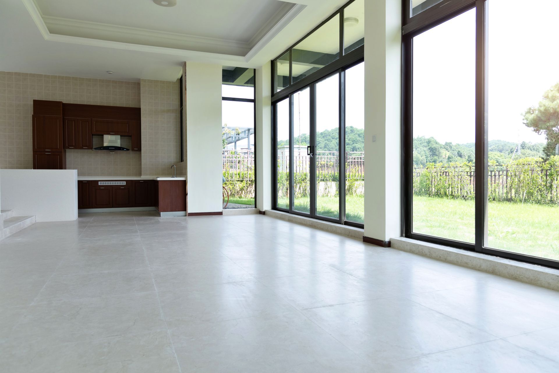 Empty modern living room with large floor-to-ceiling windows and a kitchen area