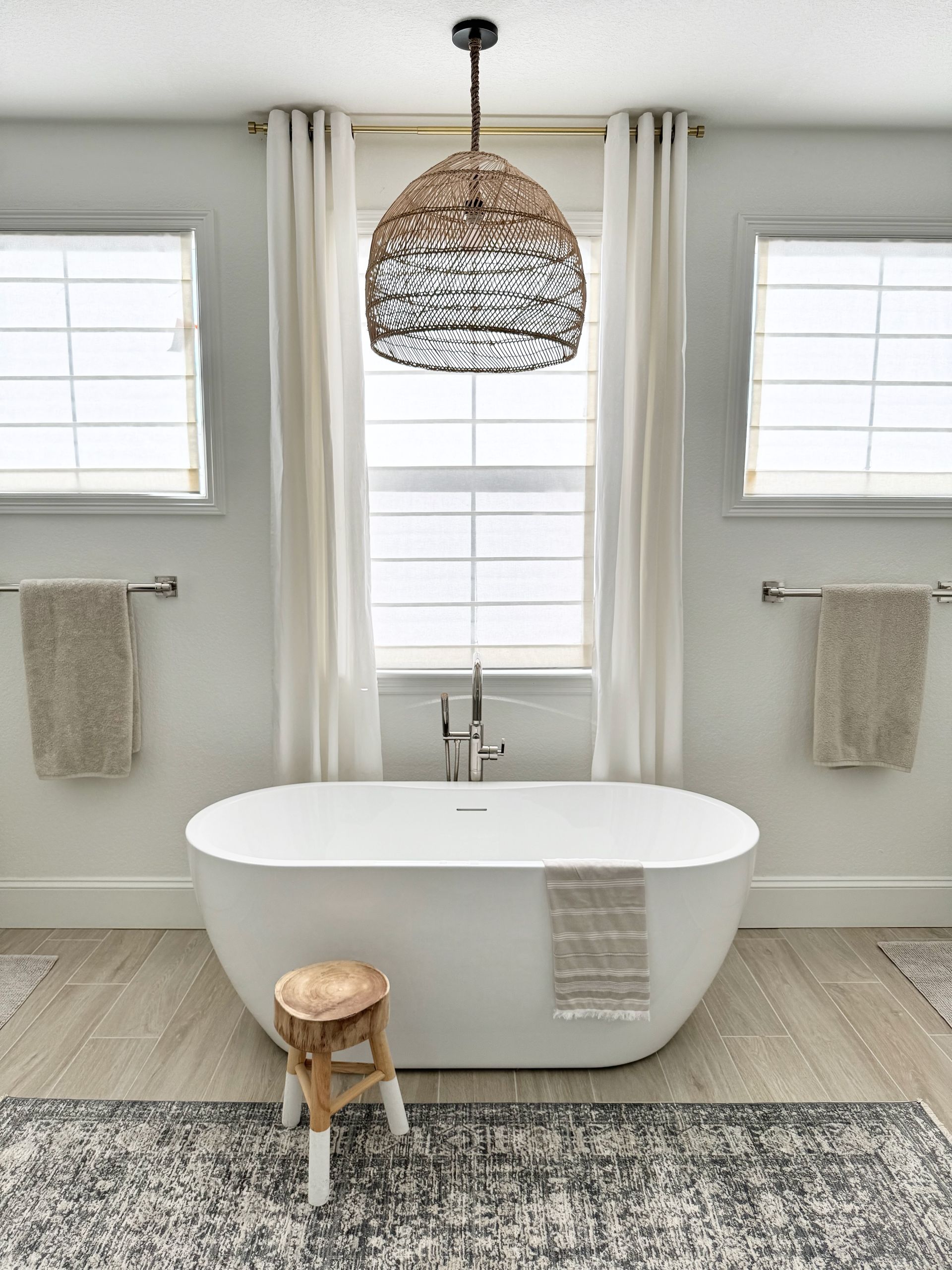 Bright bathroom with freestanding tub, woven pendant light, and neutral decor on a patterned rug.