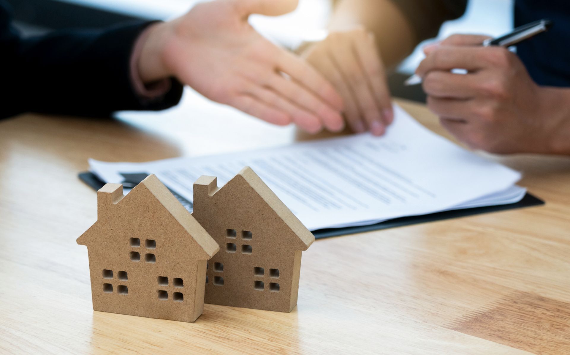 Two wooden houses are sitting on a wooden table next to a person signing a document.