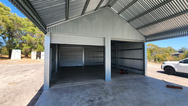 A modern, two-bay metal garage with corrugated walls and roof, situated on a concrete slab in an open, sunny outdoor area.