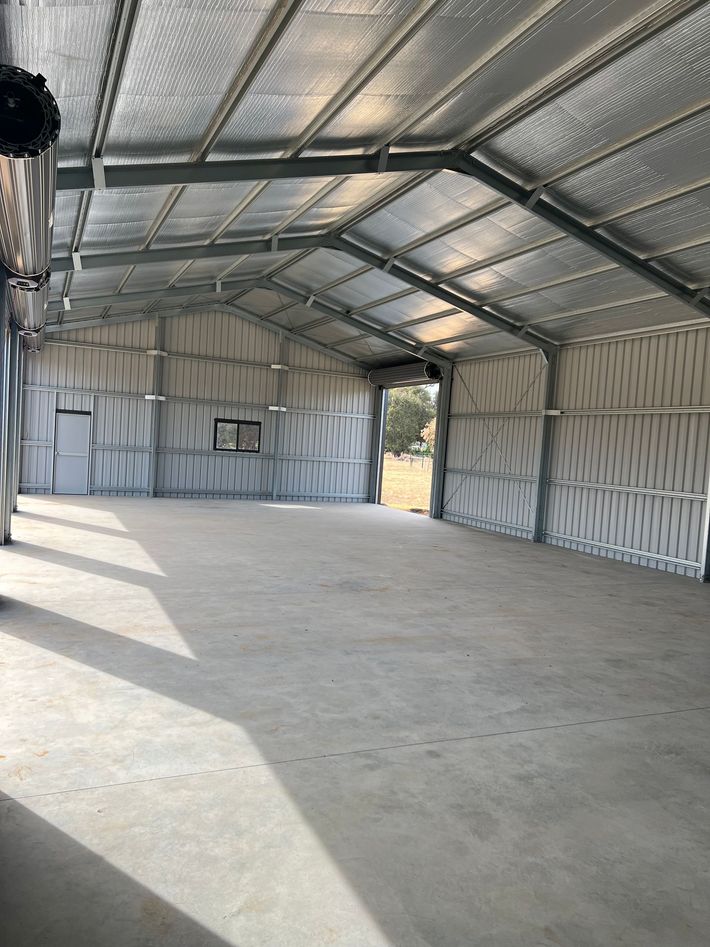 An empty, spacious metal shed with insulated walls and a concrete floor, viewed from the entrance looking outward.