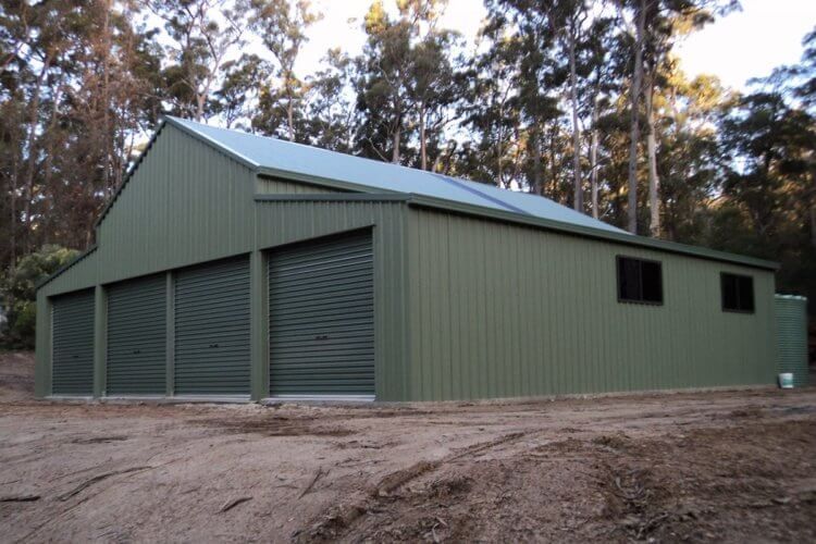 A green building with a blue roof is in the middle of a dirt field
