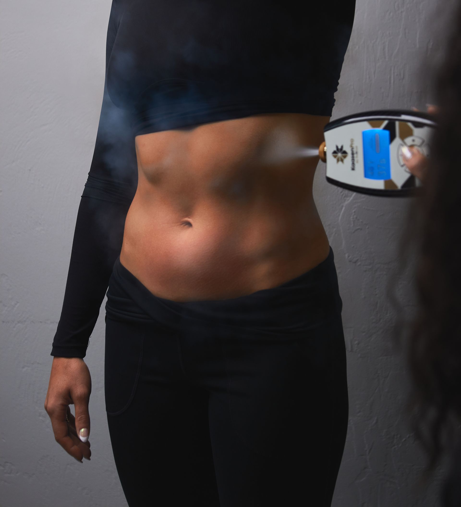 Woman's torso receiving a body sculpting treatment. A device sprays vapor on her side, near the waist.