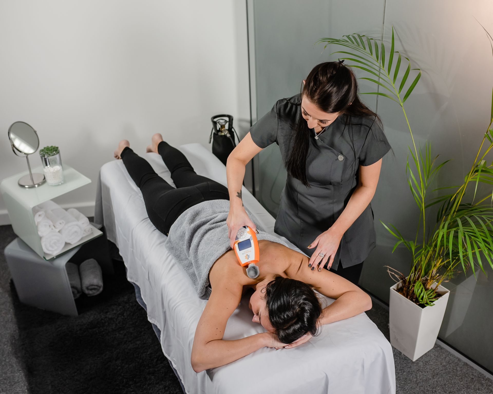 Therapist uses a device on a patient's back during a treatment session in a clinic.