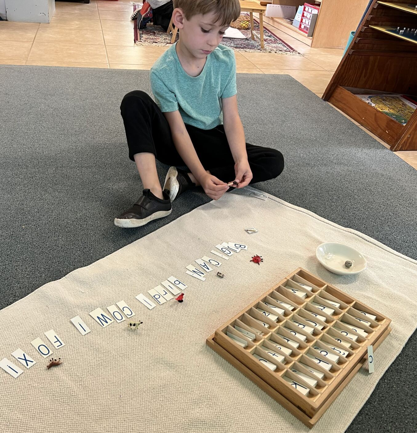 A young boy is sitting on the floor playing with montessori writing materials.