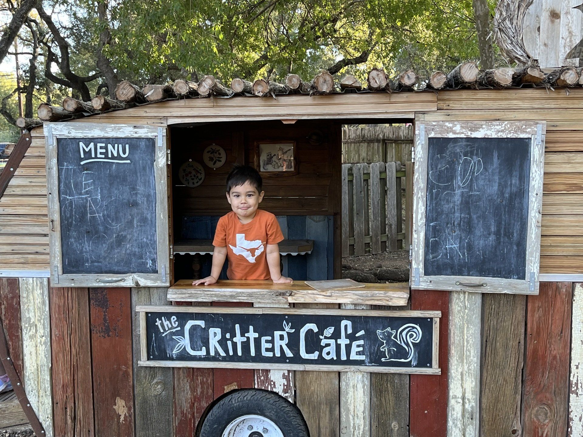 A young boy is looking out of the window of a critter cafe.