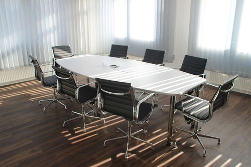 Modern conference room with a white oval table and black office chairs on a wood floor