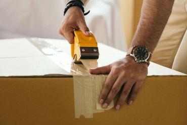Hands sealing a cardboard box with packing tape on a table