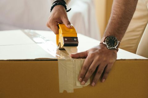 Hands sealing a cardboard box with packing tape on a table