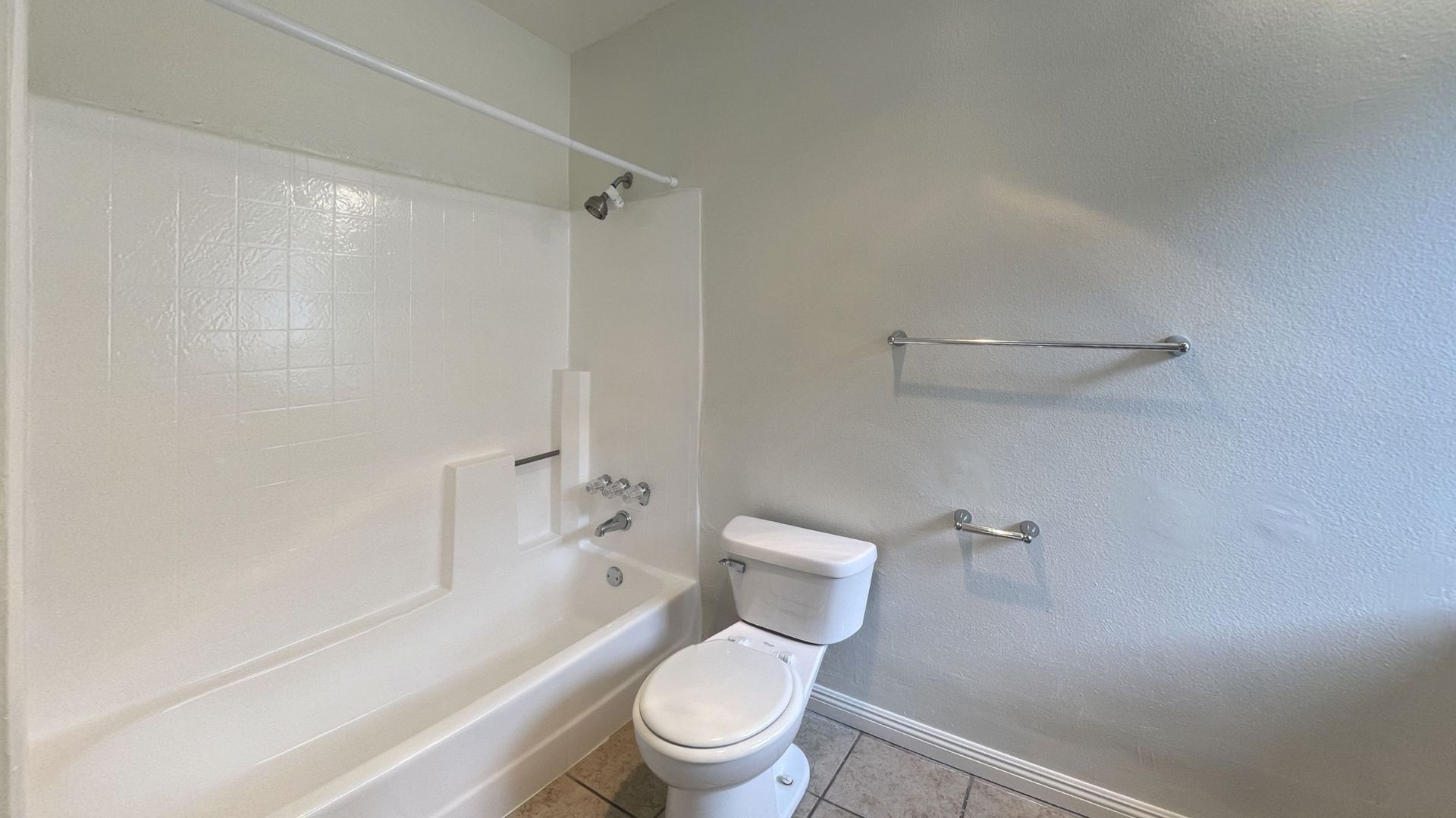 White bathroom with tub, toilet, and towel rack on textured walls.