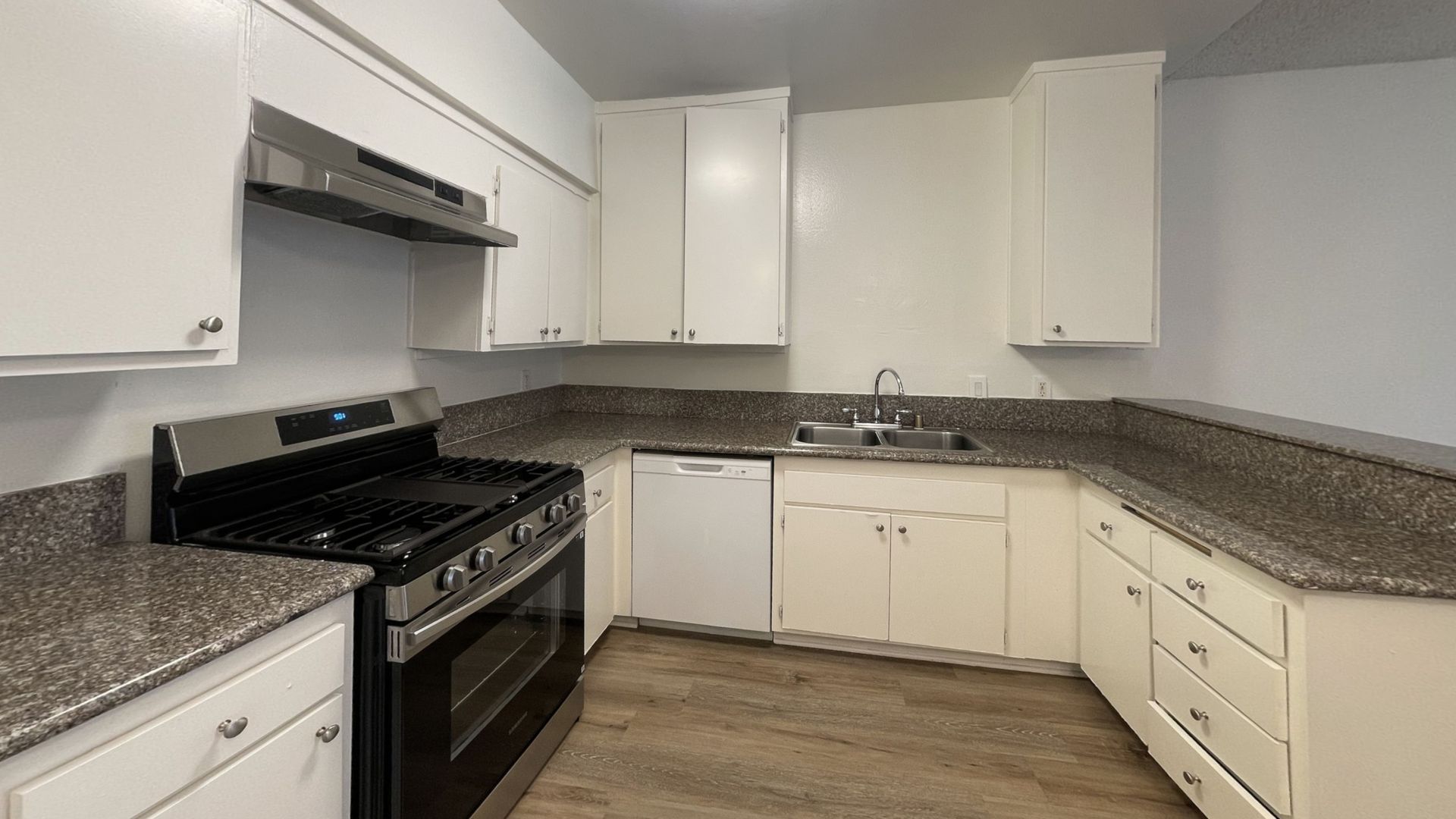 White kitchen with dark countertops, stainless steel appliances, and wood-look flooring.