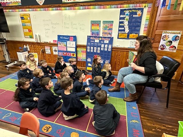 A woman is reading a book to a group of children in a classroom.